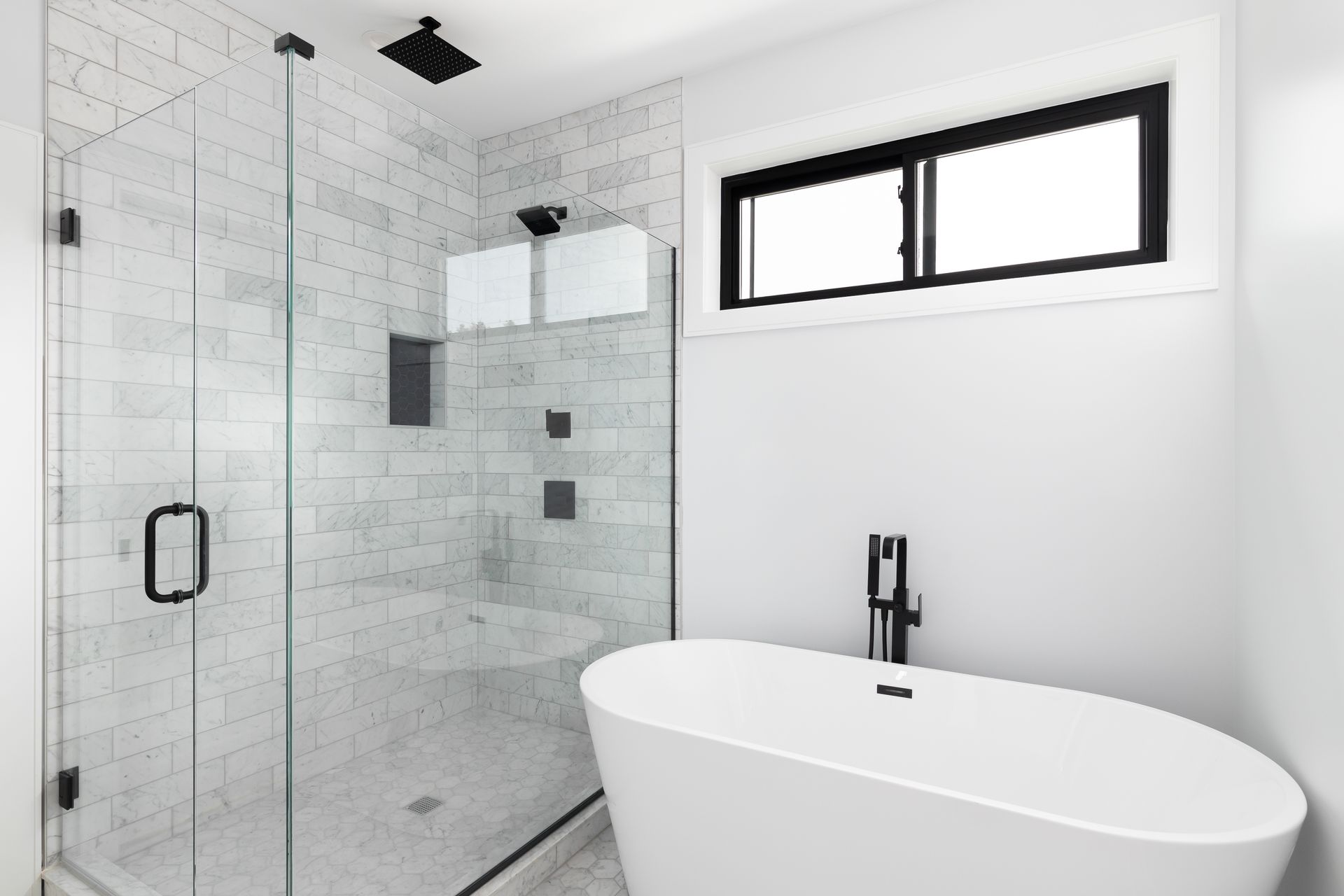 Modern shower with clear glass door, marble tile walls, and a freestanding bathtub in a bright bathr