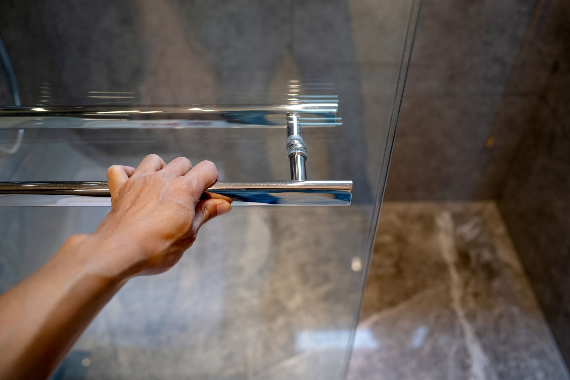 A hand pulling on a custom shower glass door from Wholesale Glass and Mirror in Fairview, NC