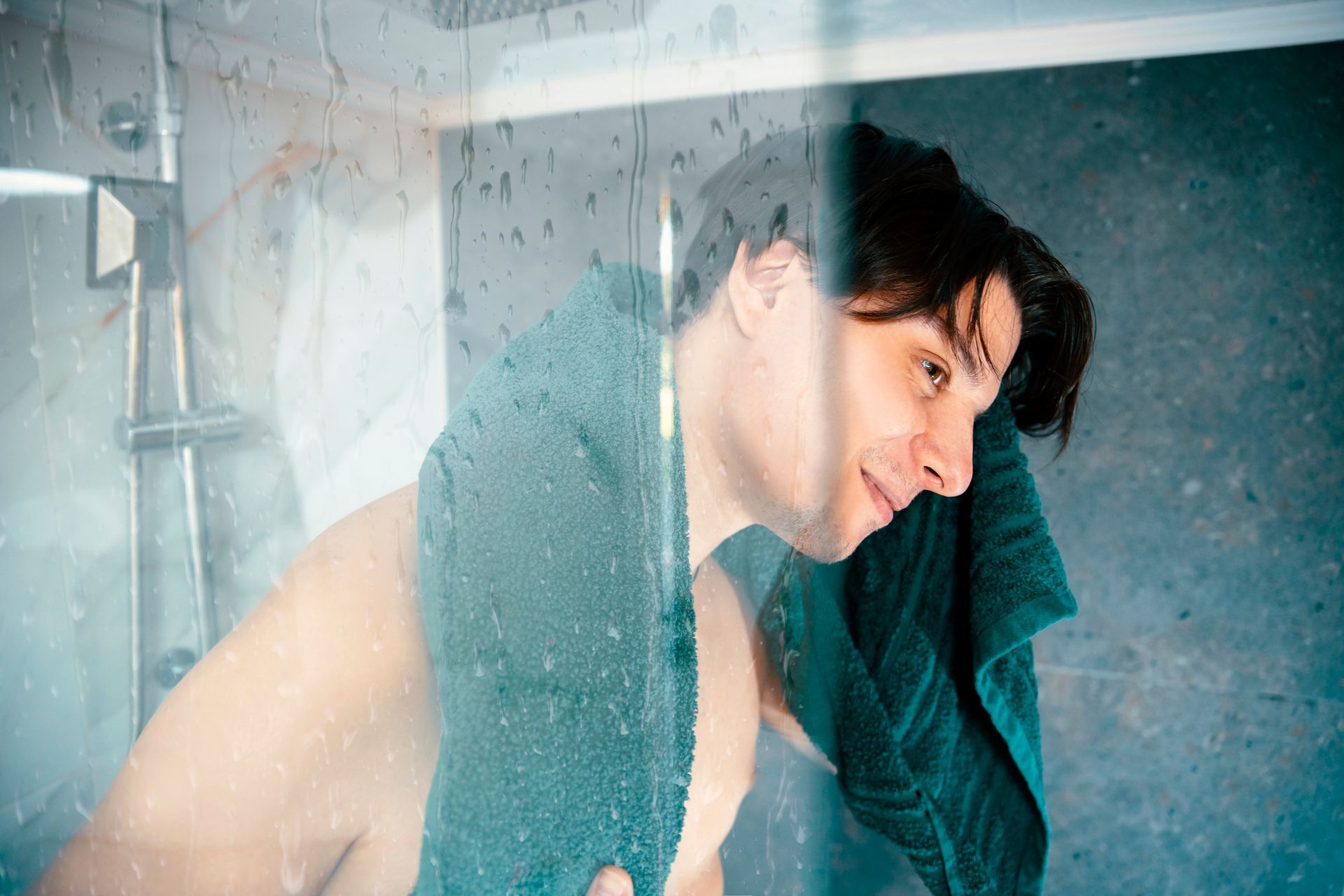 A man behind a glass shower door washing and grooming.