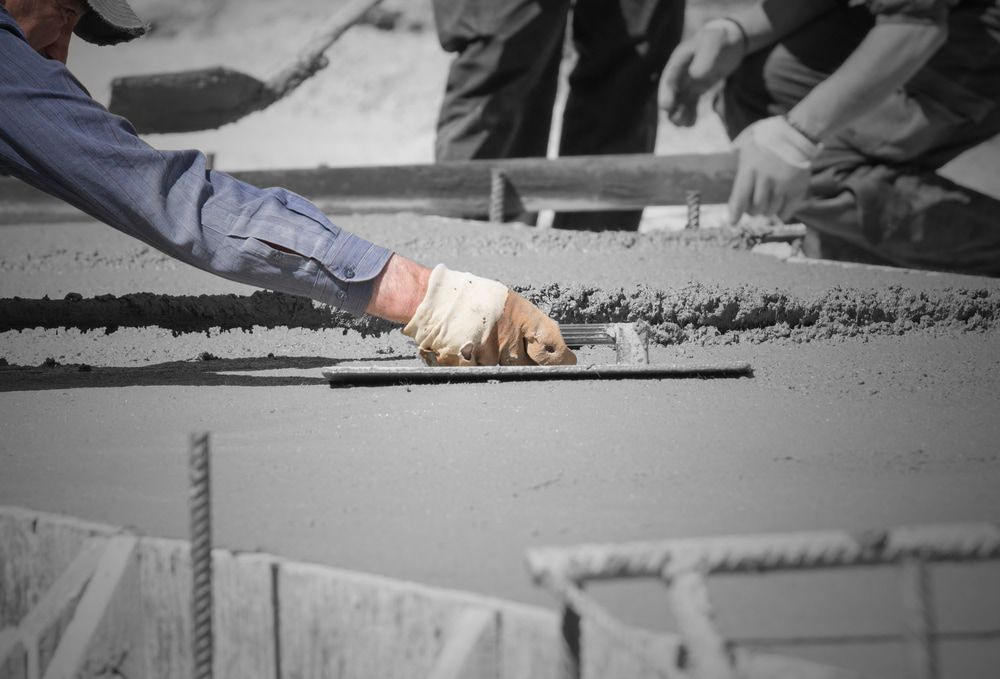 A Man is Using a Trowel to Spread Concrete on a Construction Site — Aussie Mad Pumping In Wondunna, QLD