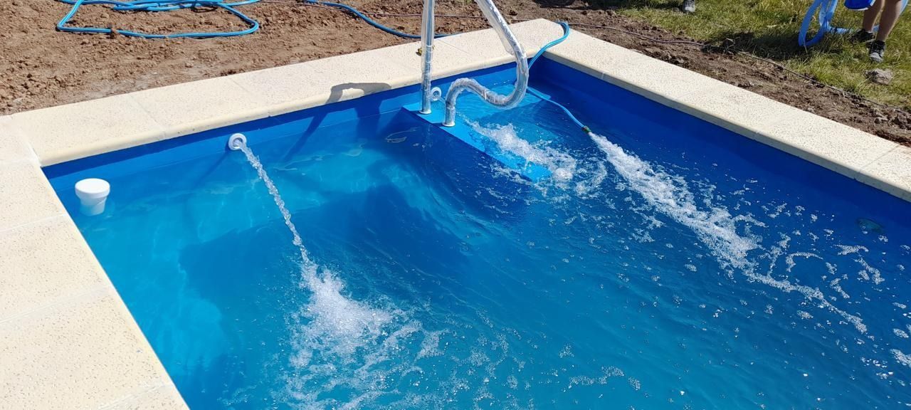 Una piscina rectangular azul con ribetes blancos. El agua fluye desde un tubo y una fuente.