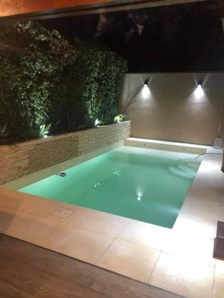 Pequeña piscina iluminada por la noche con muro de piedra y vegetación circundante.
