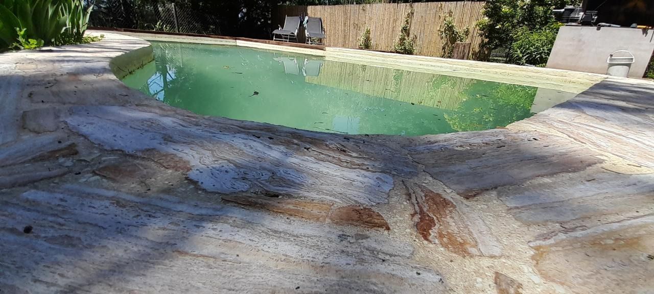 Piscina con borde de piedra y agua verde. La luz del sol proyecta sombras sobre el borde de piedra.