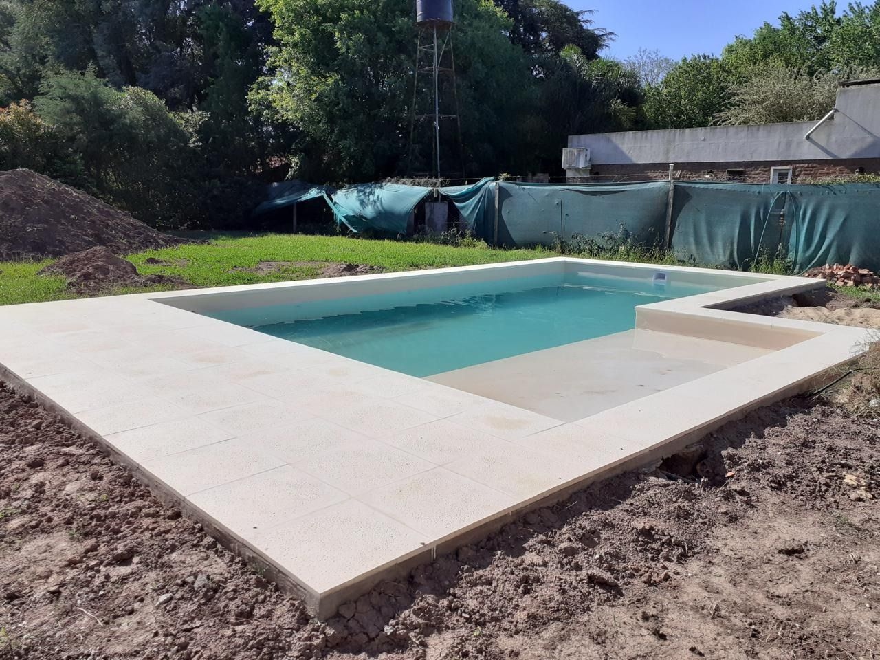 Una piscina rectangular con marco de hormigón de color claro, situada en un patio trasero.