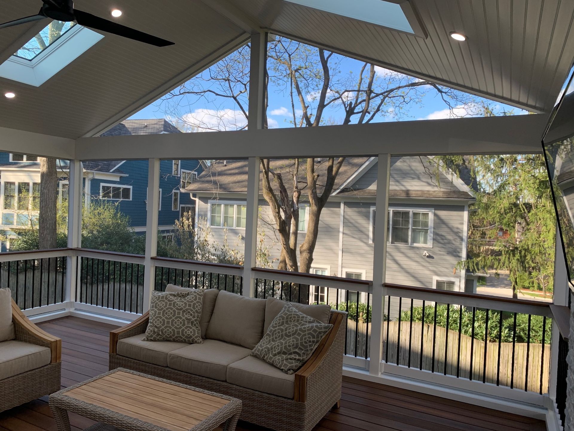 A screened in porch with a couch , chairs , table and skylight.