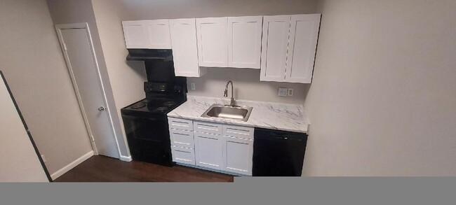 A kitchen with white cabinets , black appliances , a sink and a stove.