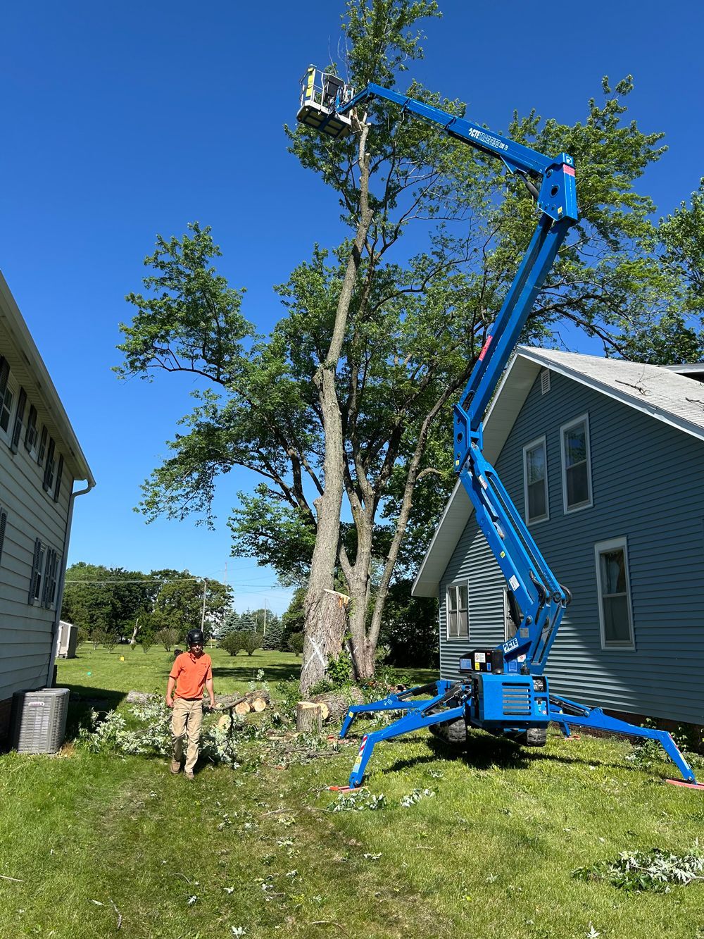 A man is standing next to a crane cutting a tree in front of a house.