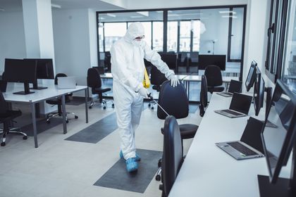 Un homme en tenue de protection désinfecte un bureau avec un flacon pulvérisateur.