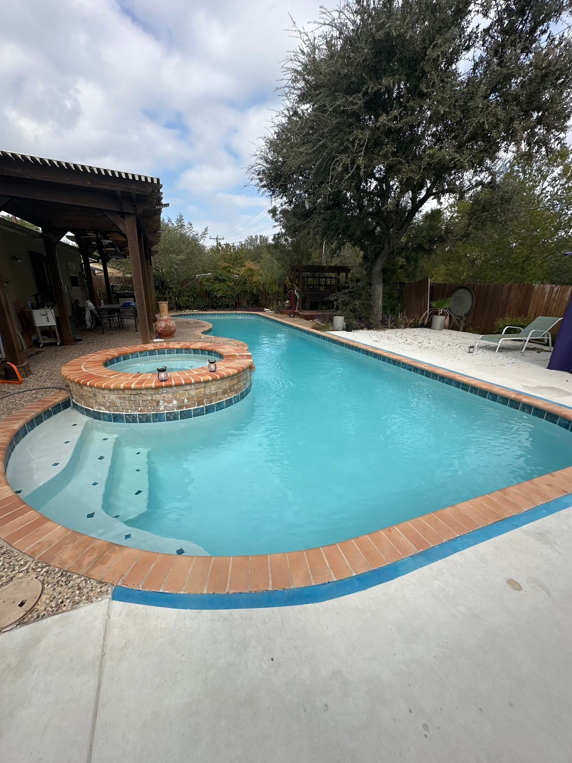 Backyard pool with a circular hot tub, white lounge chairs, and a shaded patio under trees.