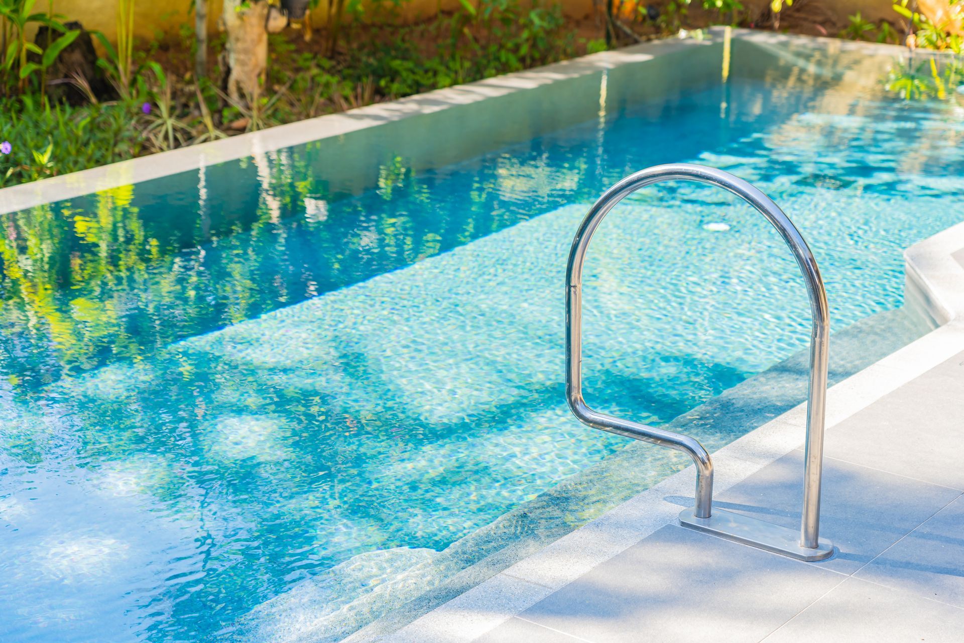 Outdoor swimming pool with clear blue water and a metal pool ladder by the edge