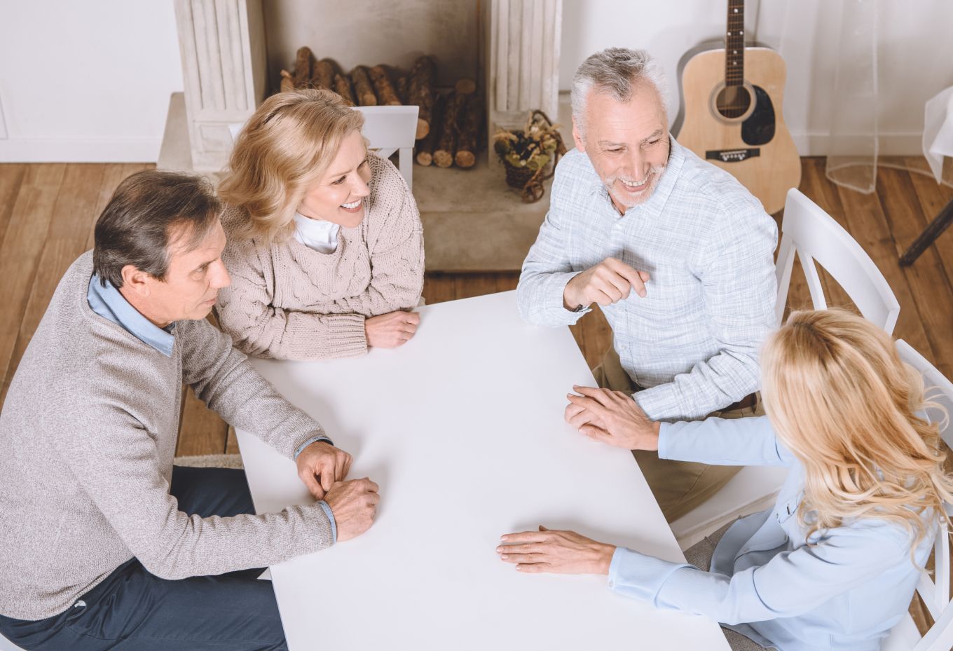 Four people in a bright room talking around a table with guitars in the background