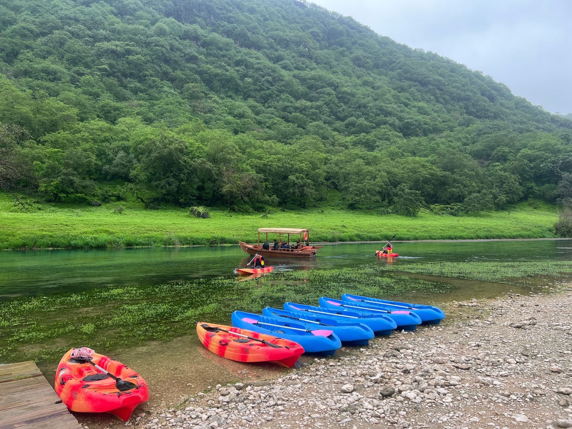 Arabian Wanderers travelers kayaking on the peaceful waters of Wadi Darbat in Salalah, Oman, surrounded by lush green mountains during the Khareef season