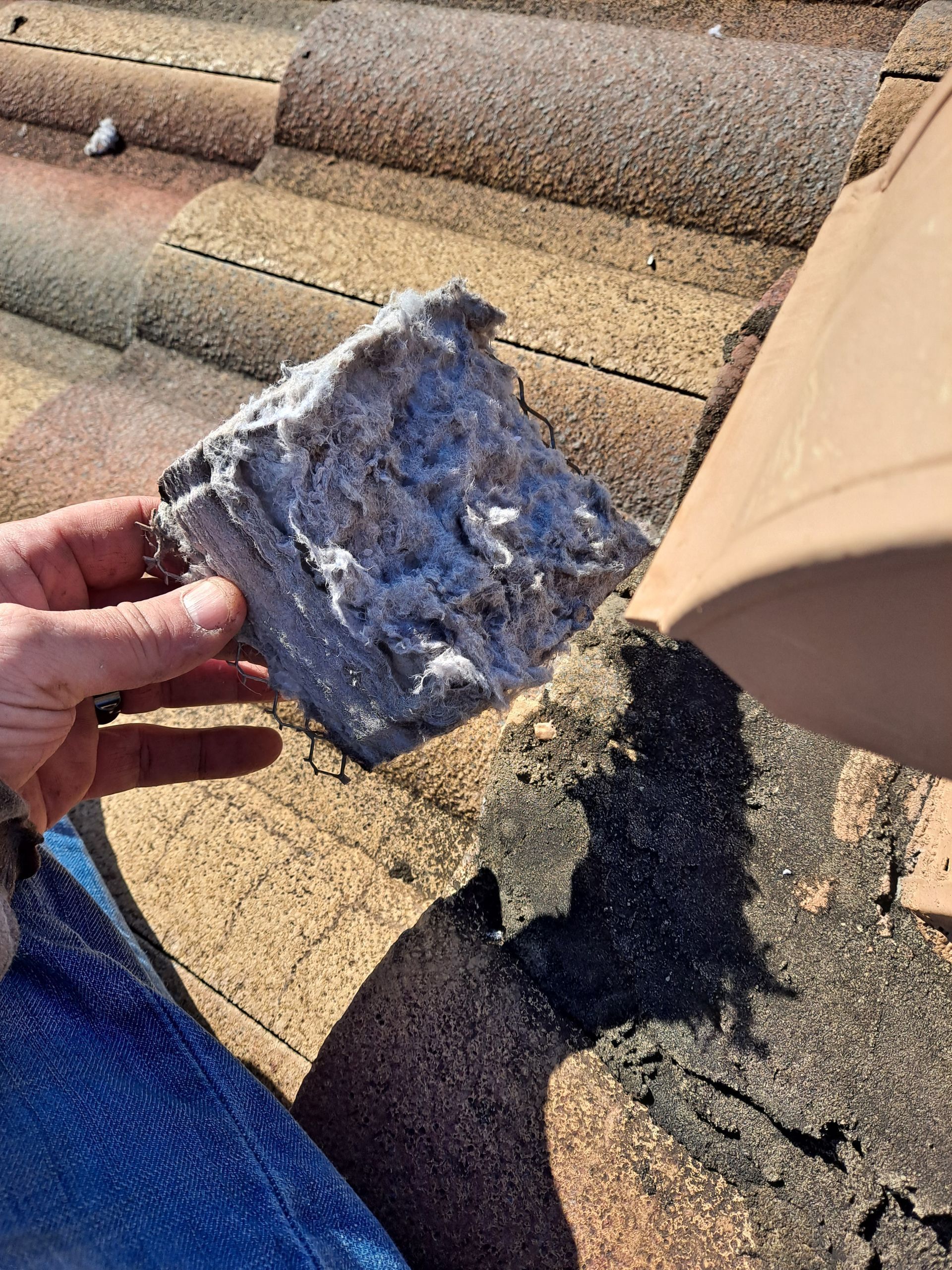 Hand holding a gray, crumbling block near a terracotta tile roof.