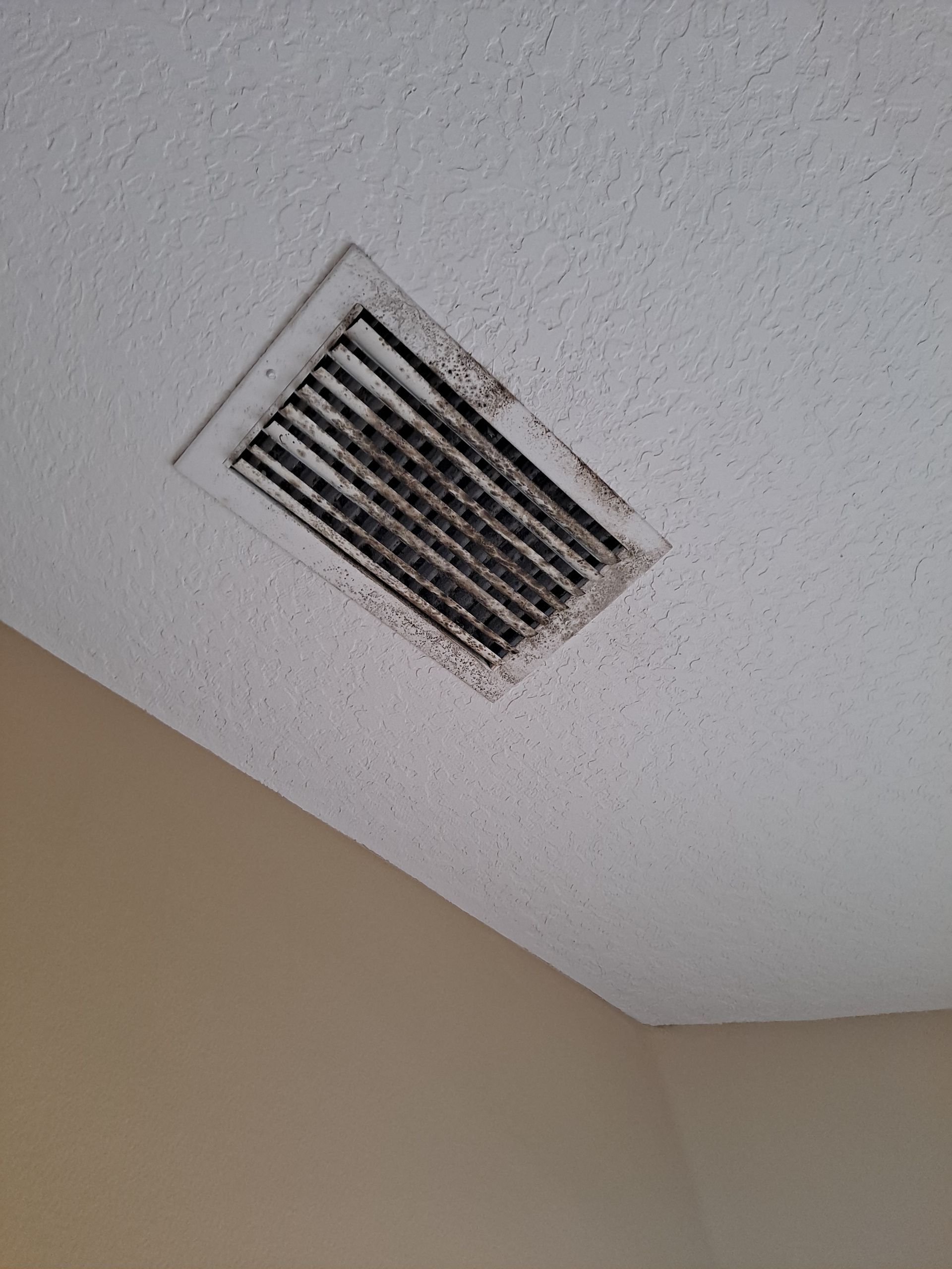 A dirty air vent on the ceiling of a room.