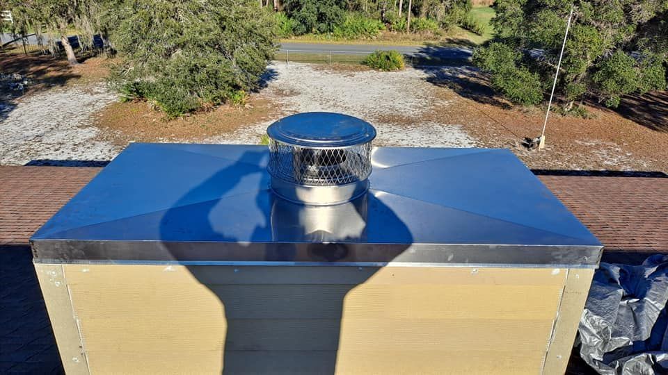 A stainless steel chimney on top of a roof with trees in the background.