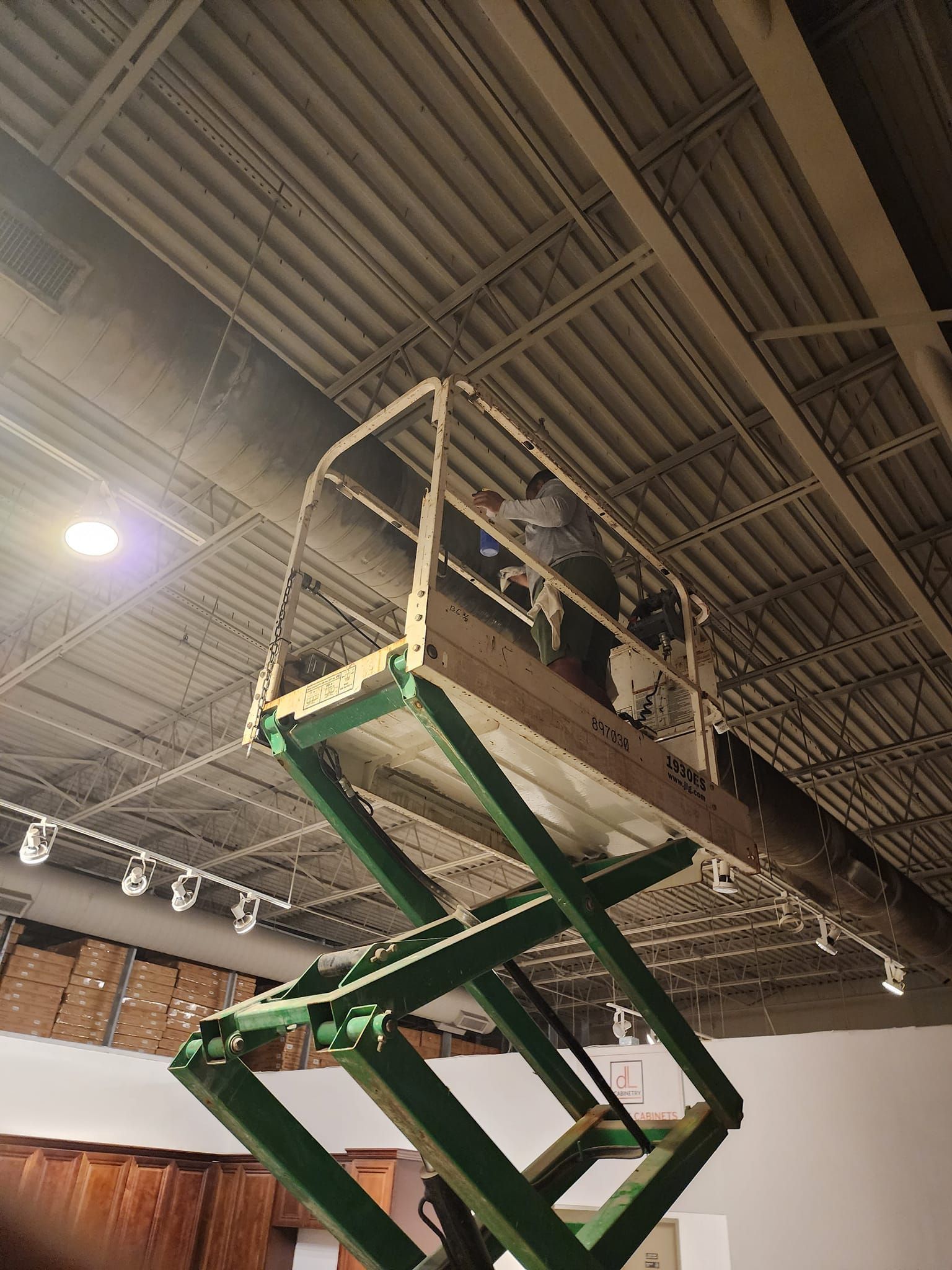 A man is standing on a green scissor lift working on a ceiling.