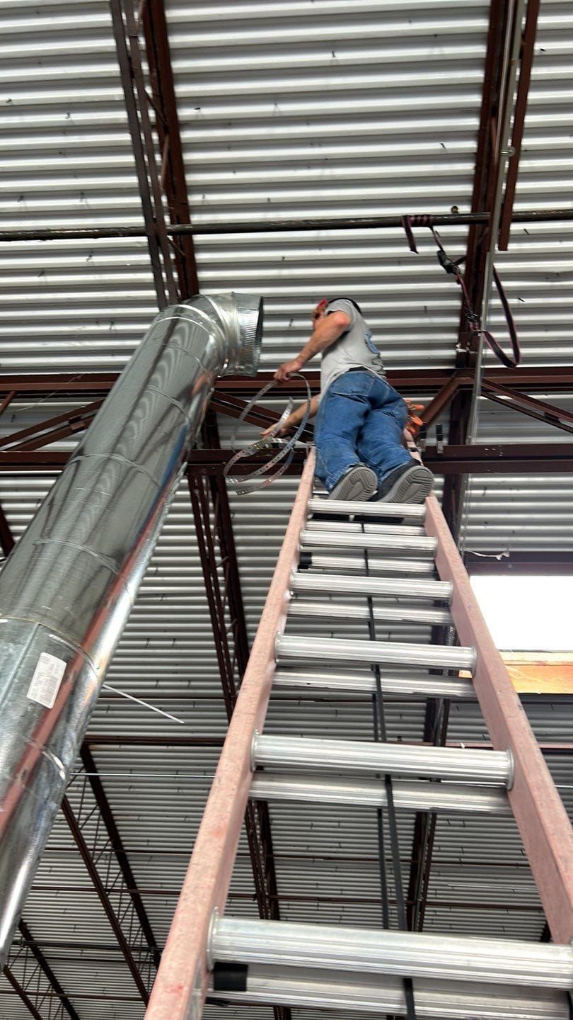 Man on ladder working near HVAC duct in a building under construction.