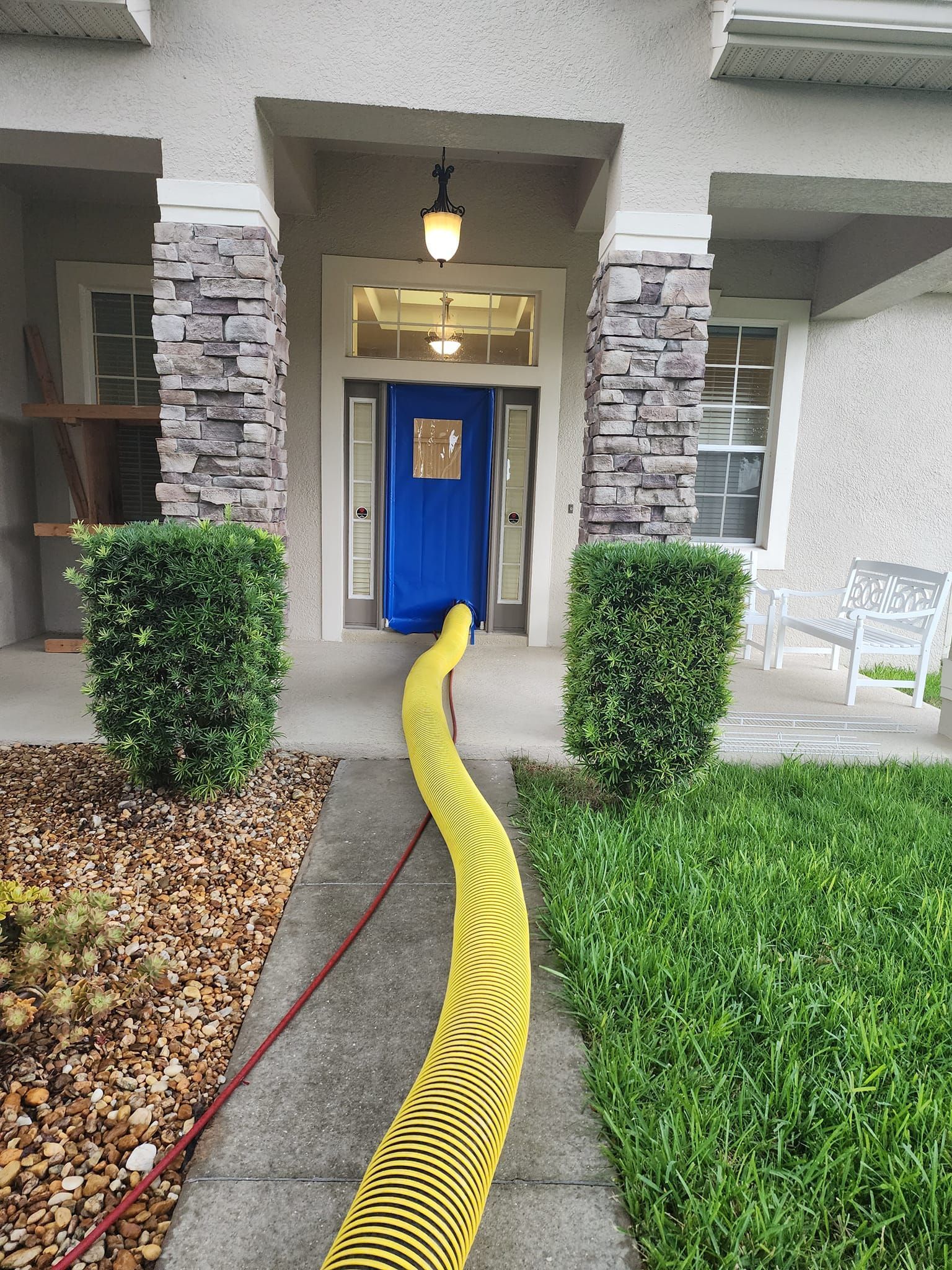 A yellow hose is sitting on the sidewalk in front of a house.