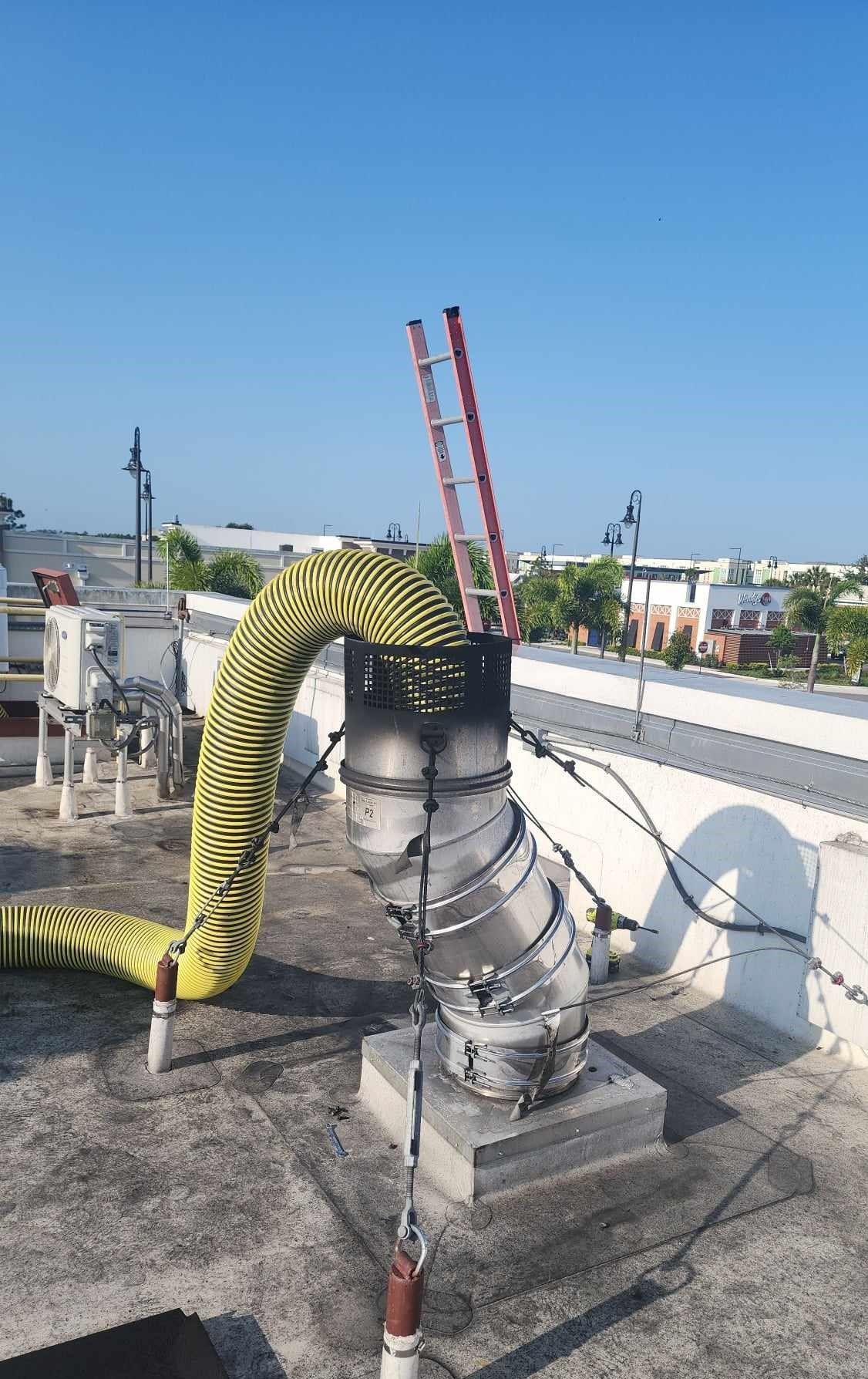 A ladder is attached to a pipe on the roof of a building.