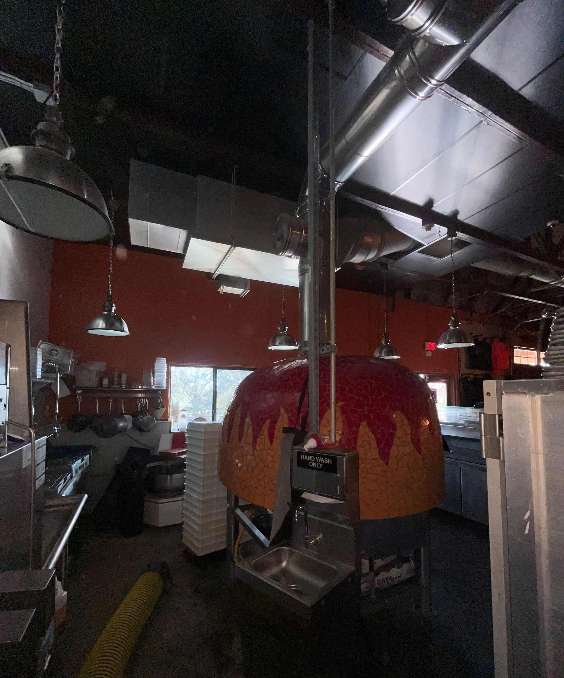 Interior of a pizza restaurant. A large, domed pizza oven is center, stainless steel kitchen on left.