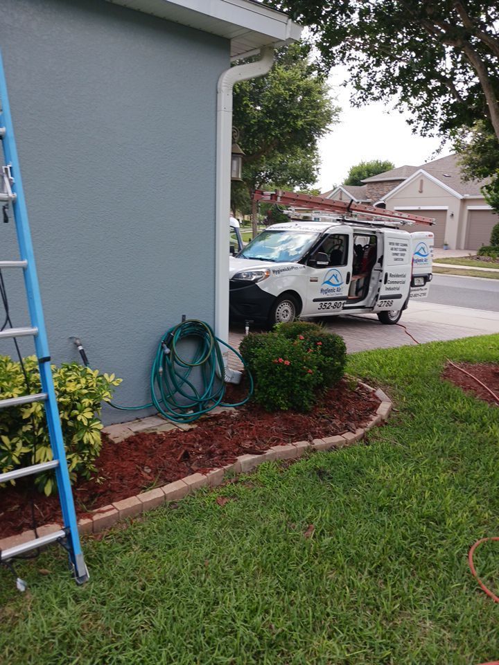 Blue house exterior with service van, ladder, and hose on a green lawn.