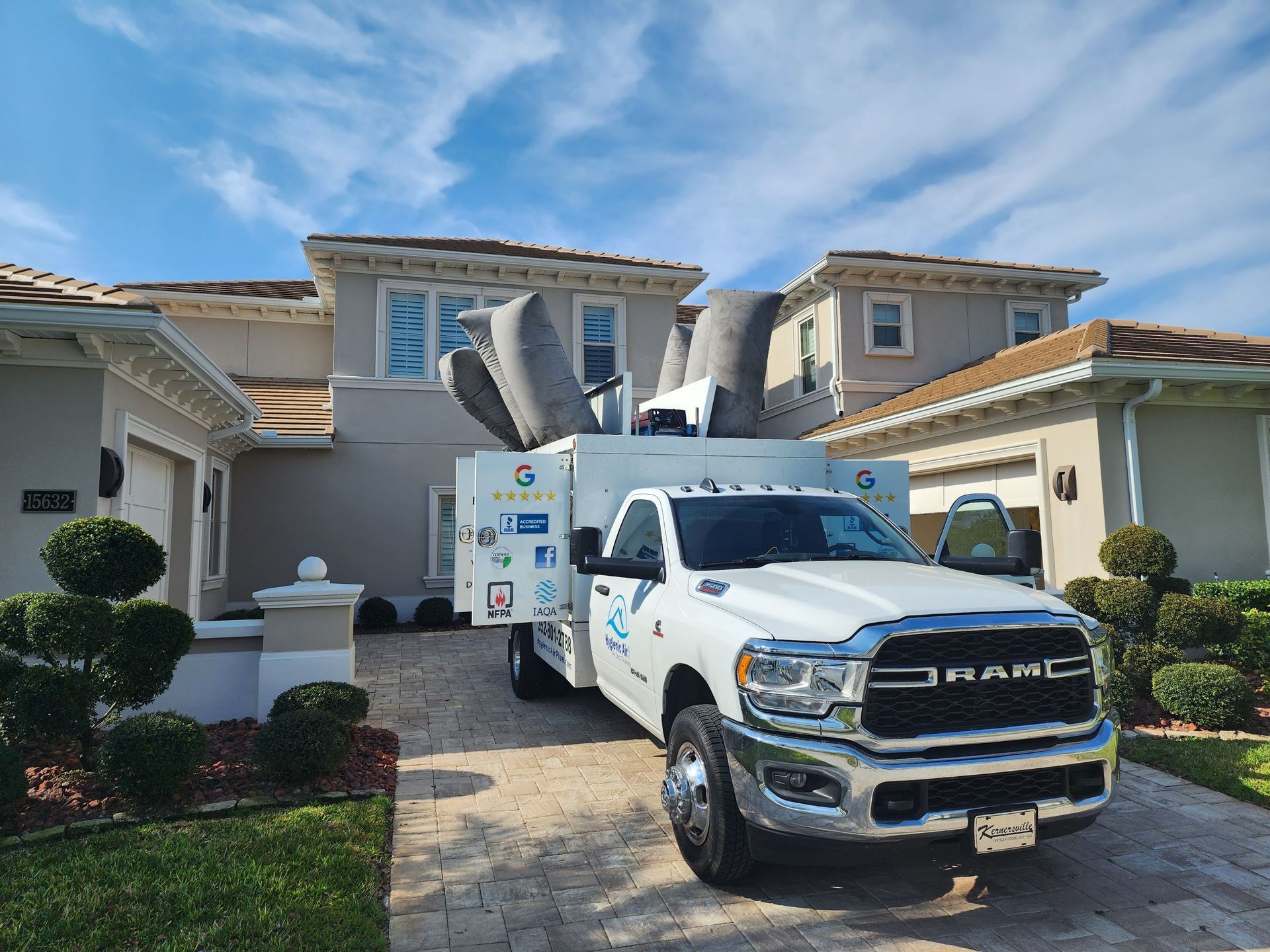 White truck with equipment parked in front of a house on a sunny day.