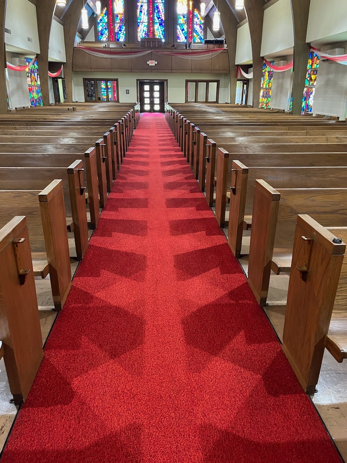 The inside of a church with rows of wooden benches and a red carpet.