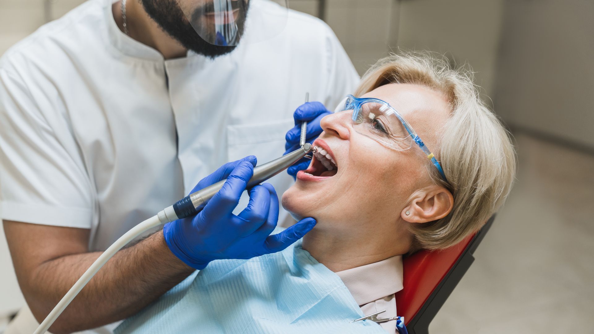 A woman is sitting in a dental chair getting her teeth examined by a dentist.