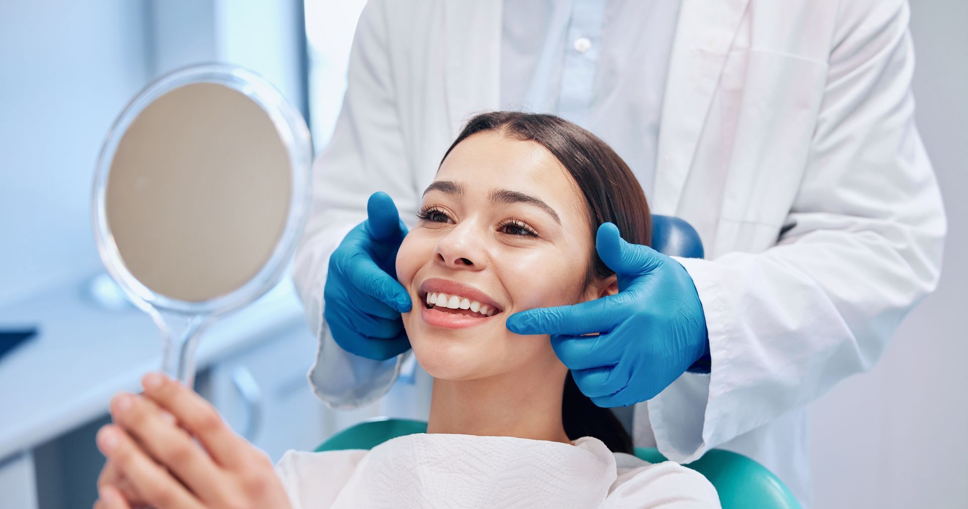 A woman is sitting in a dental chair while a dentist examines her teeth.