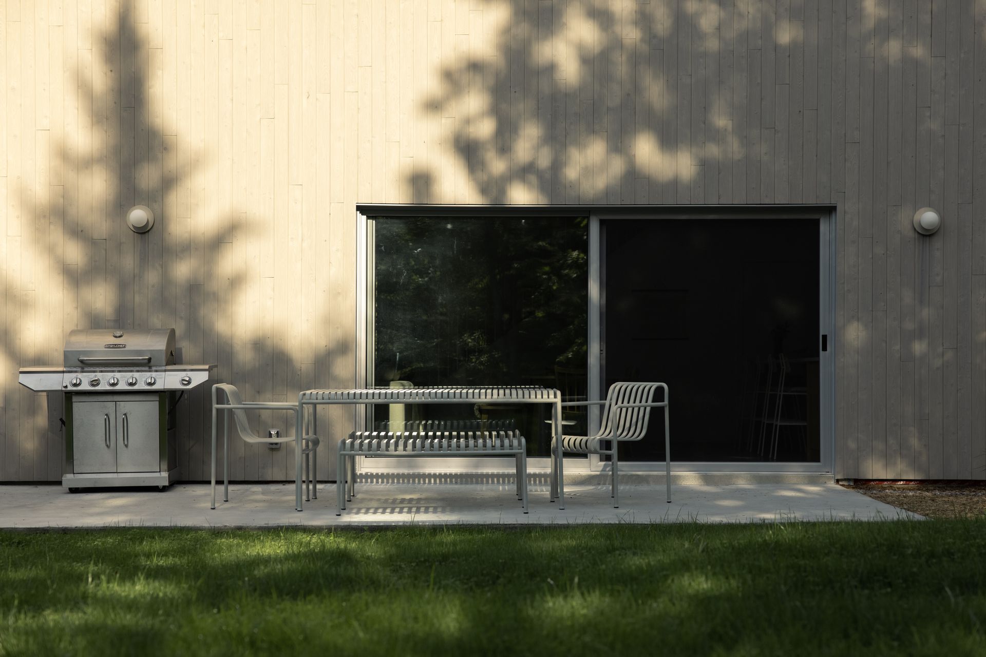 Un patio avec une table et des chaises et un grill devant une maison.