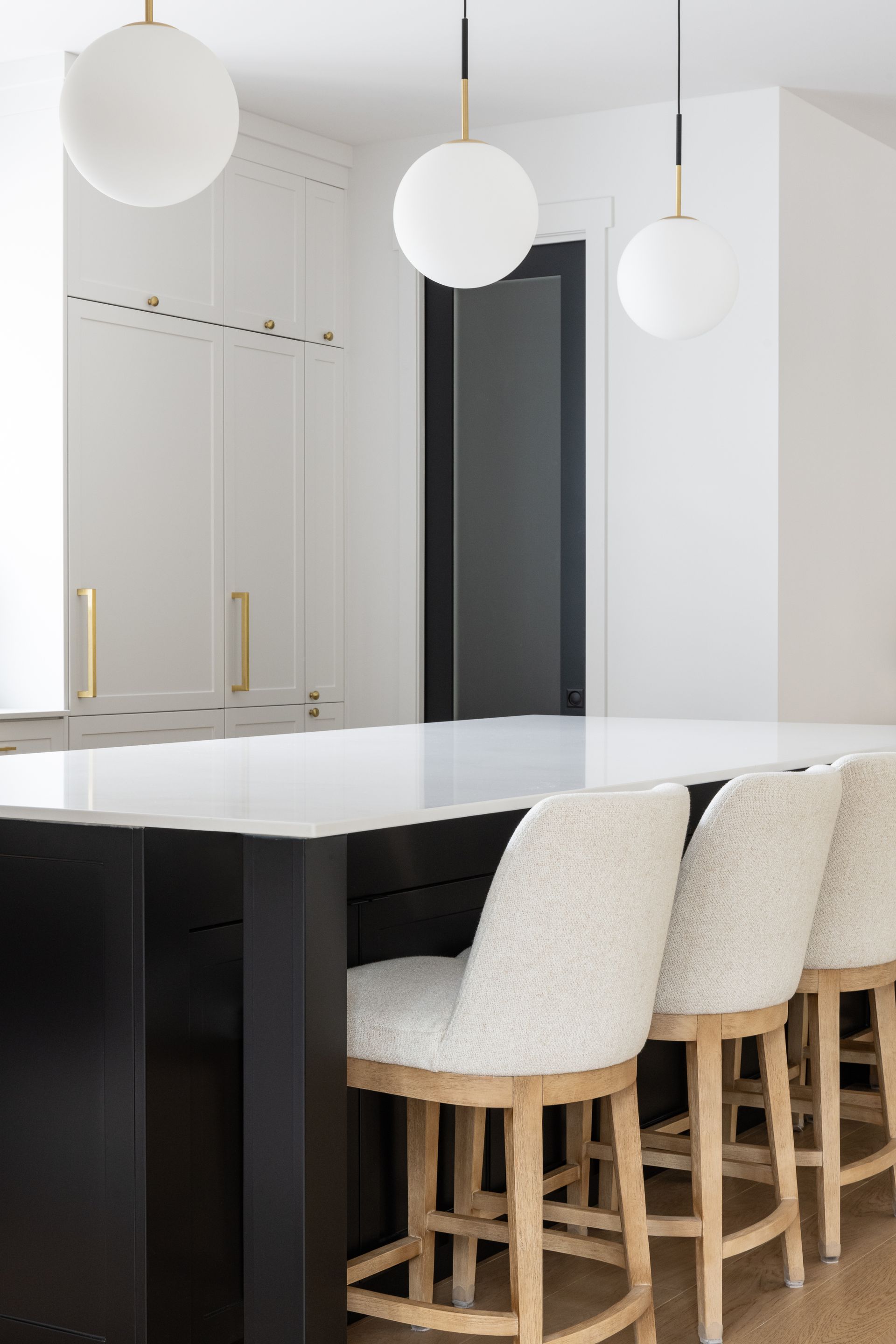 Une cuisine avec un îlot noir, des comptoirs blancs et des chaises blanches.