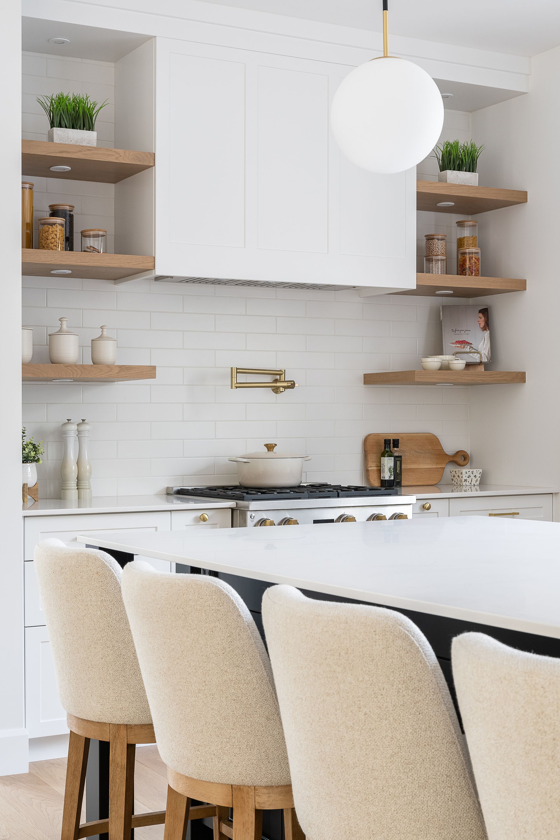 Une cuisine avec des armoires blanches, des tabourets, une cuisinière et un évier.