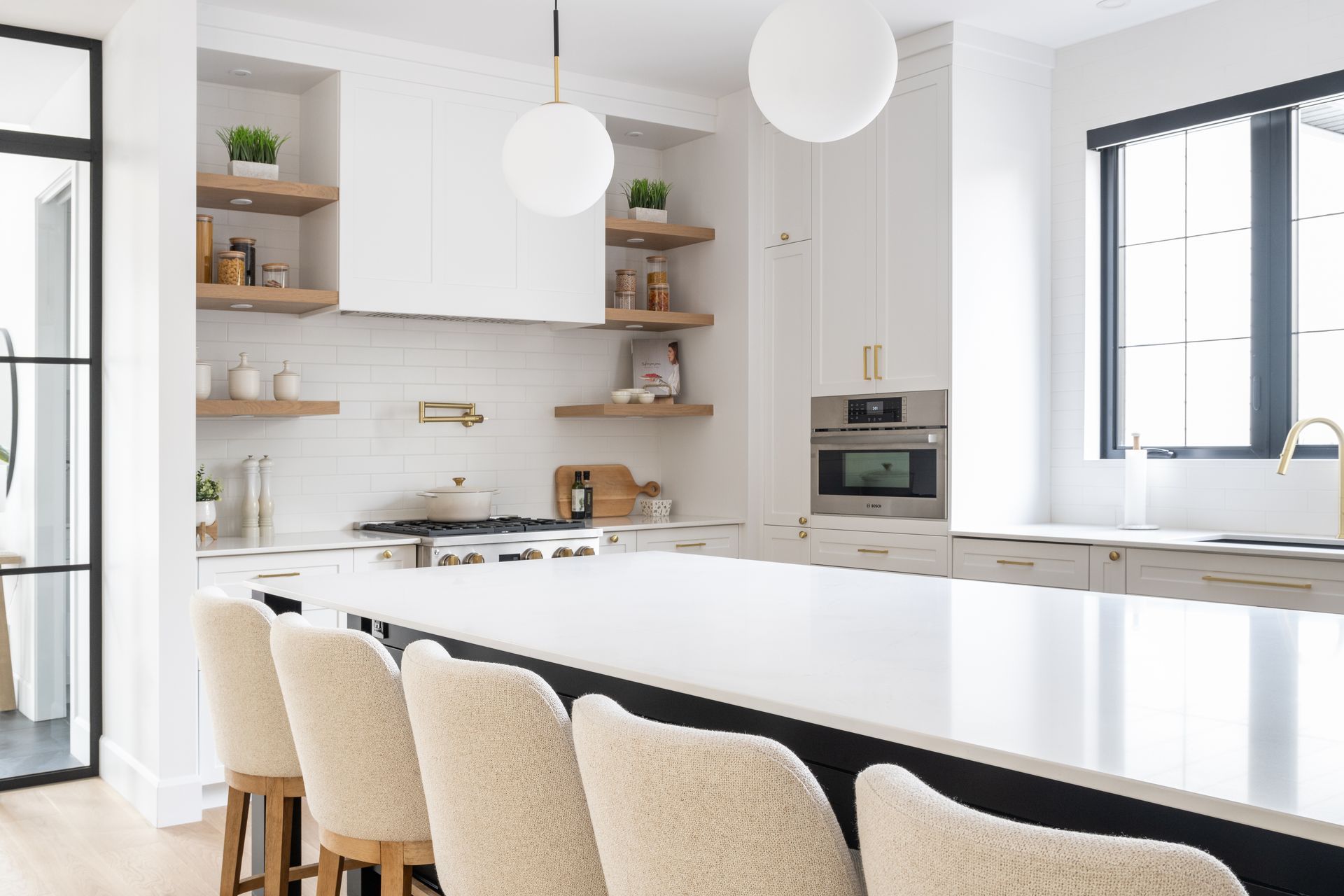 Une cuisine avec armoires blanches, un grand îlot, des tabourets et une fenêtre.