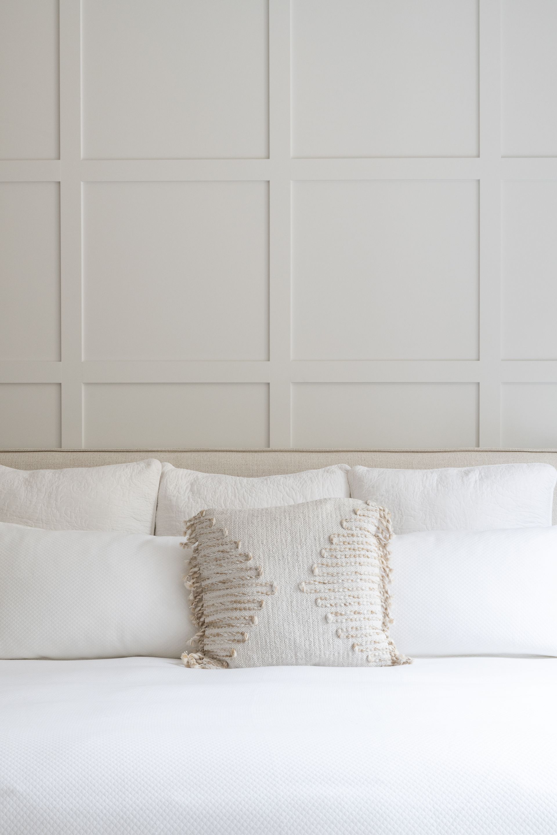 Un lit avec des draps et des oreillers blancs dans une chambre avec un mur blanc.
