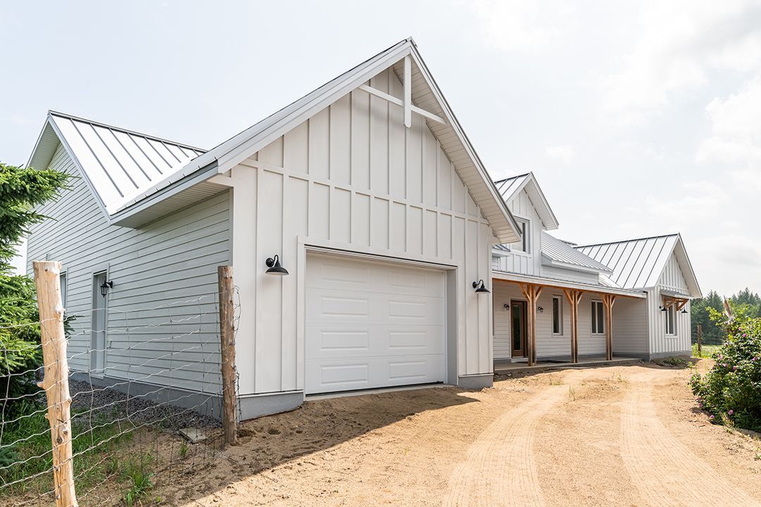 Une maison blanche avec un garage et un toit en métal se trouve au sommet d'un chemin de terre.