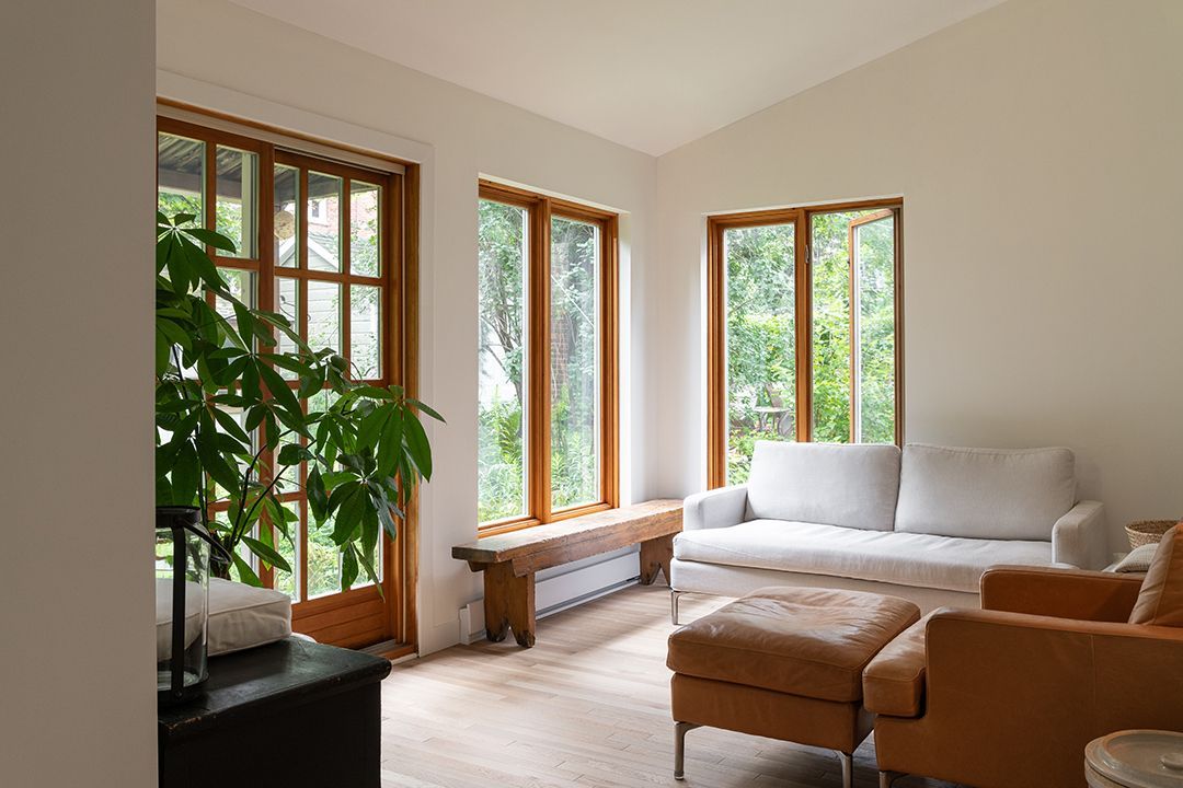 Un salon avec un canapé, des chaises, un pouf et beaucoup de fenêtres.