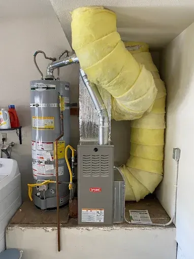 A water heater and a furnace unit with large, yellow-insulated vent pipes sitting on a raised platform in a utility room.