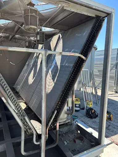 A view inside an industrial air conditioning unit, showing a large, slanted metal coil assembly and a fan motor.