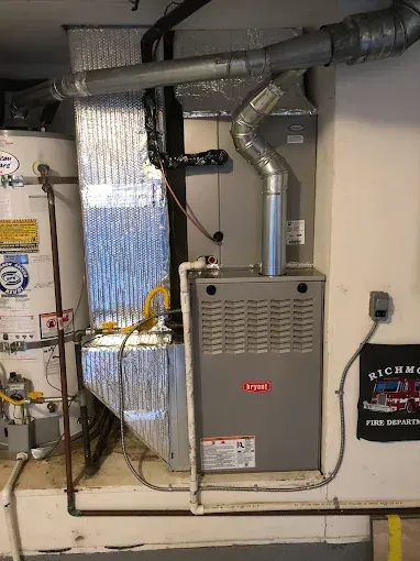 A grey Bryant furnace and silver foil-insulated ductwork in a basement next to a white water heater.