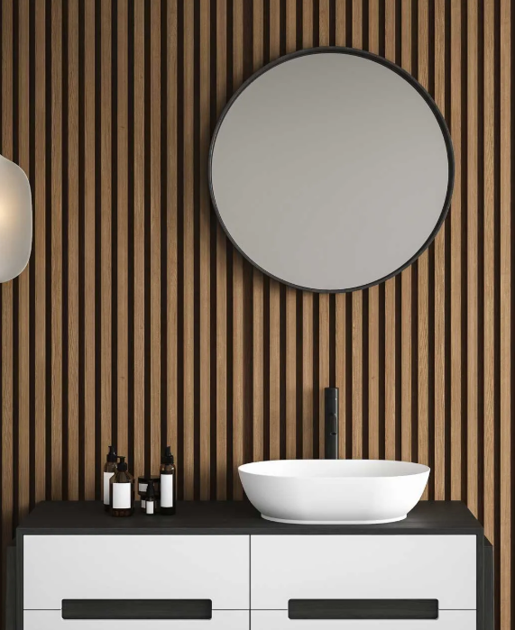 Baño con espejo redondo, lavabo sobre encimera, mueble oscuro y revestimiento de madera en la pared.