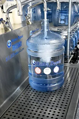 A large water jug being filled from a tap at a Water Depot station.
