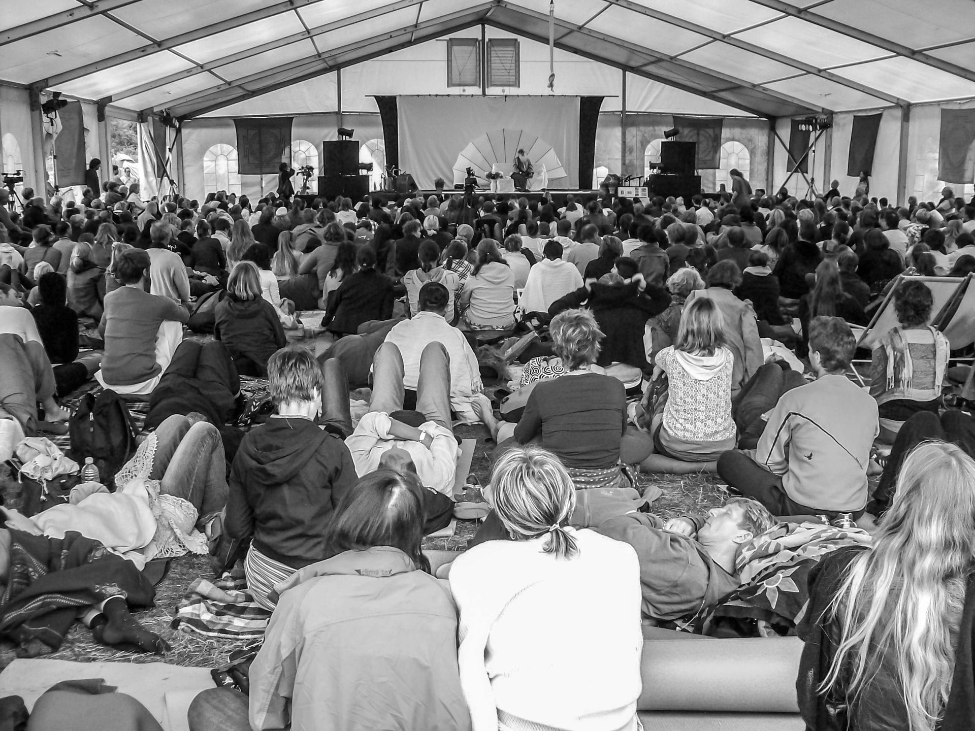Large crowd seated inside a tent, watching a presentation on stage.