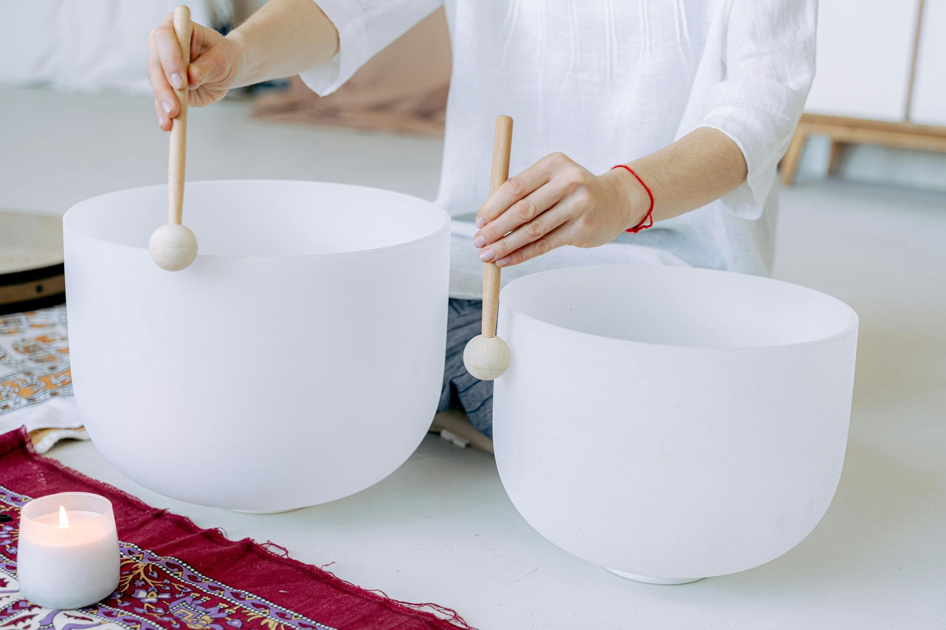 Person playing crystal singing bowls, white room, soft lighting.