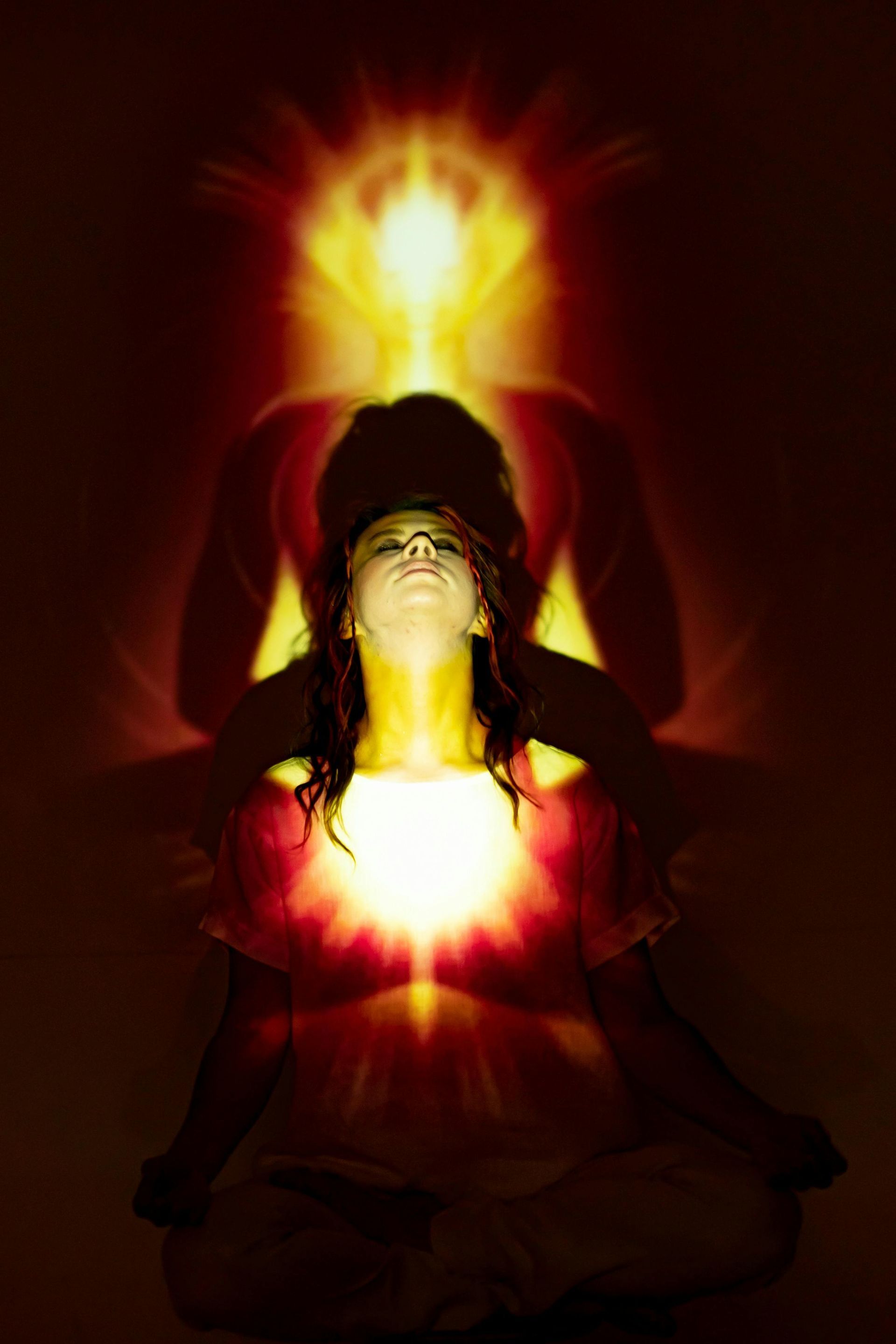 Woman in meditation pose, bathed in golden light. Silhouette of a figure above.