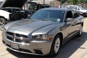 A silver dodge charger is parked in a parking lot with its hood up.