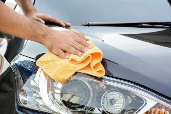 A person is cleaning a car with a yellow cloth.