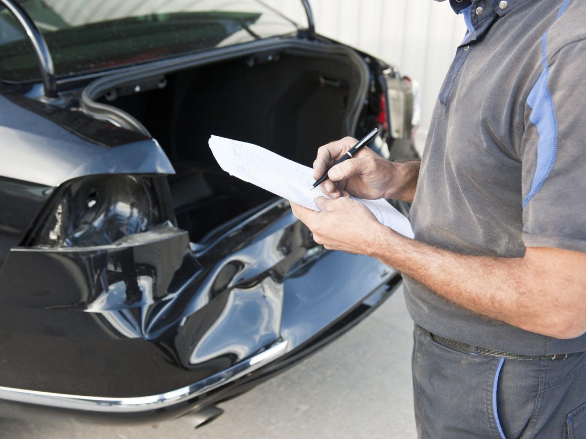A man is writing on a piece of paper in front of a damaged car.
