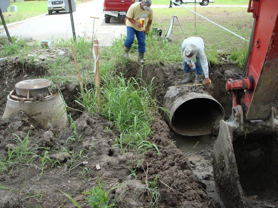 Two men are working on a pipe in the dirt.
