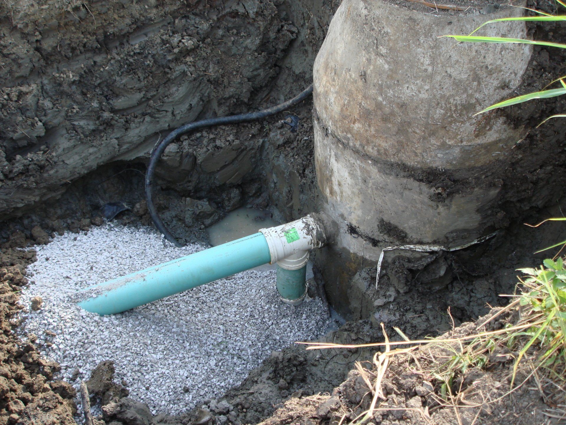 A green pipe is connected to a concrete pipe in the dirt