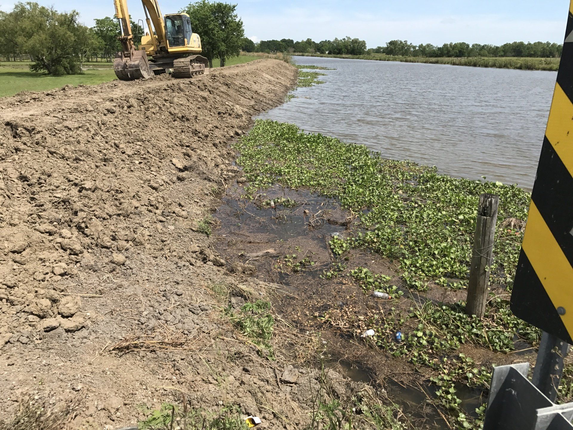 A yellow excavator is working on a dirt road next to a body of water.